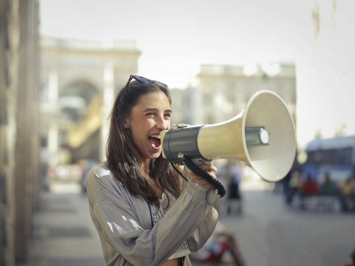 Cheerful young woman speaking into megaphone