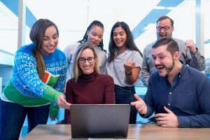 men and women sitting and standing while looking at laptop