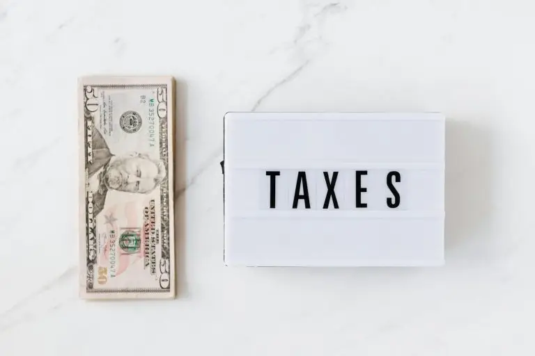Overhead view of a fifty-dollar bill and a lightbox with 'TAXES' on a marble surface.