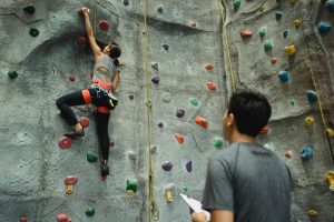 female rock climbing wall while man watches