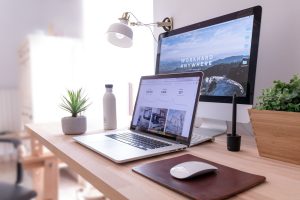 Laptop and computer monitor on table beside white computer mouse