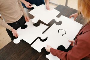 Four people assemble large white puzzle pieces on a table.