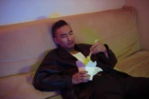 A man on a couch eating noodles with chopsticks