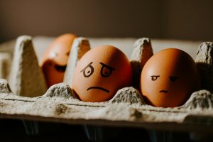 sad and happy faced brown eggs in an egg carton