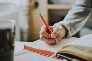 A person writing in a notebook with a red ballpoint pen