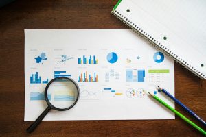 Charts and graphs with magnifying glass and stationery on wooden table