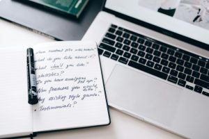 A notebook with handwritten notes next to a laptop on a workspace desk