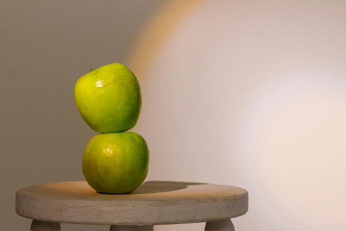 Two green apples stacked on a wooden stool