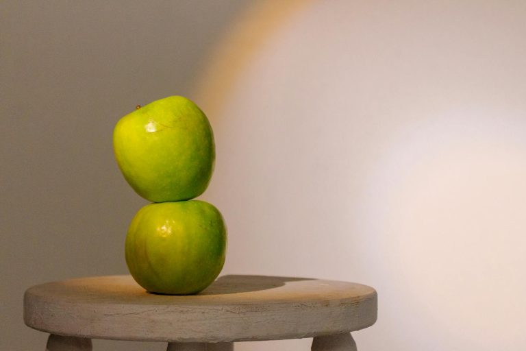 Two green apples stacked on a wooden stool