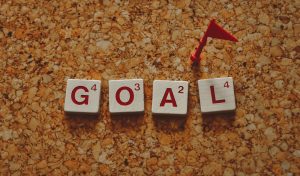 Wood tiles forming the word 'goal' with a small red flag on a cork board