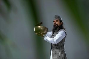 Man standing in traditional attire holding a golden bowl